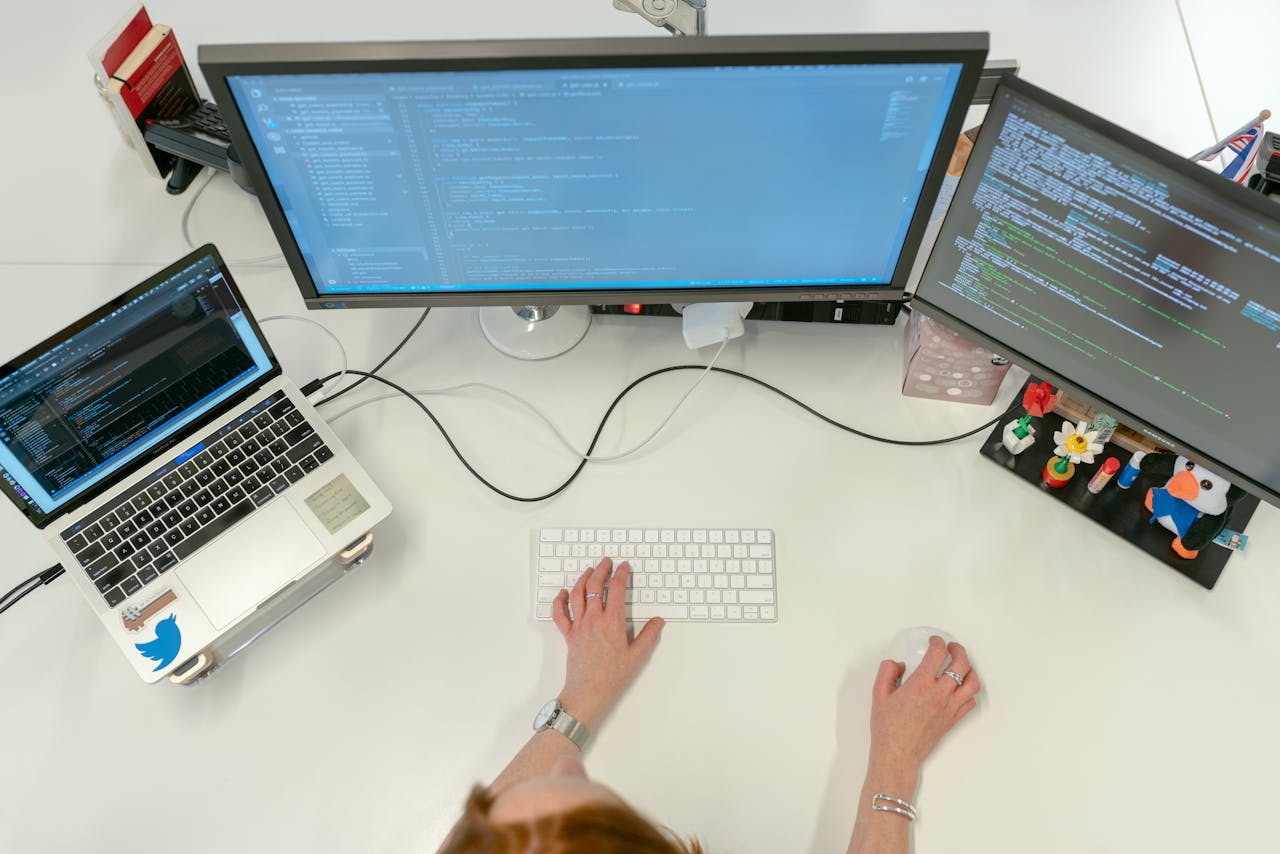 home-hero A female software engineer coding on dual monitors and a laptop in an office setting.